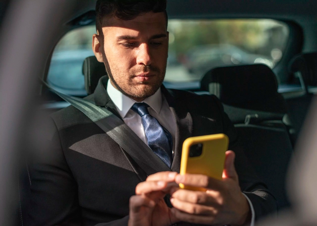 Man zit achterin in een taxi, glimlacht, en houdt een mobiel met een gele hoesje vast.